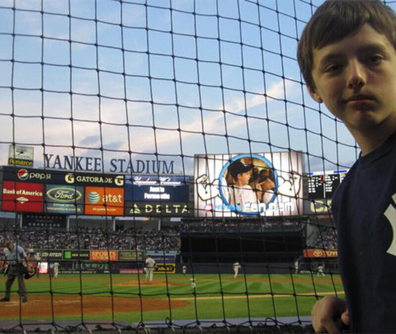 A boy standing in front of a baseball field.