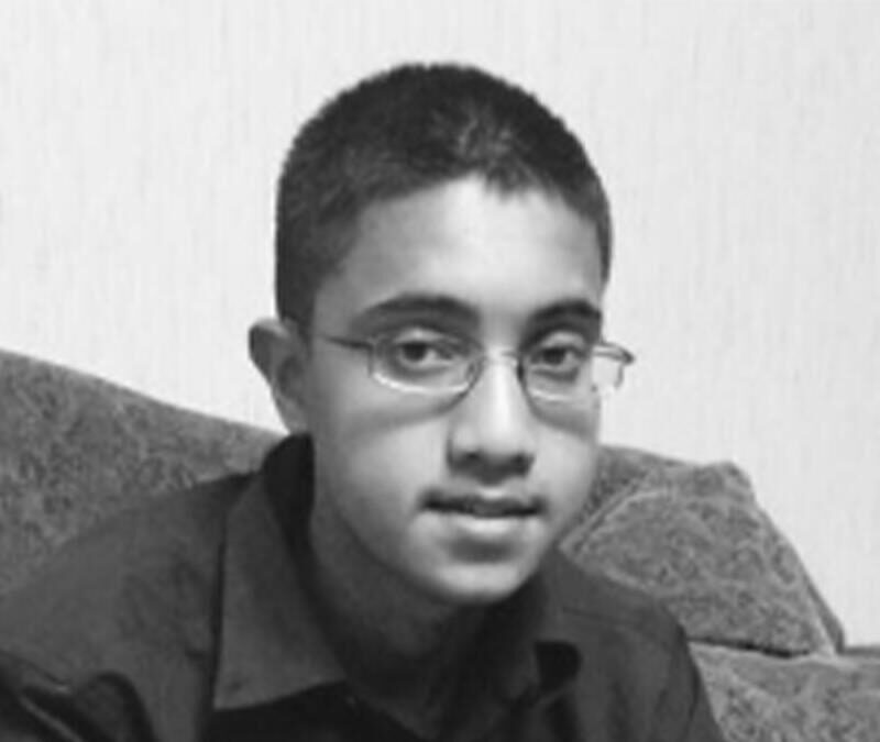 A black and white photo of a young man sitting on a couch.