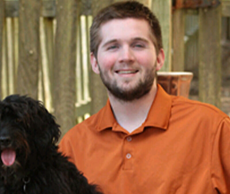 A man in an orange shirt with a black dog.