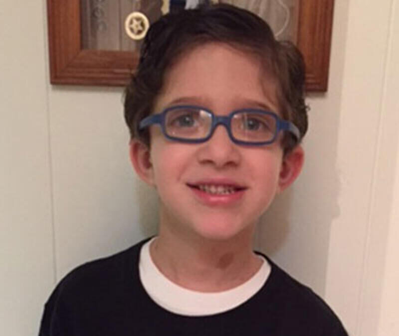 A young boy wearing glasses is smiling for the camera.