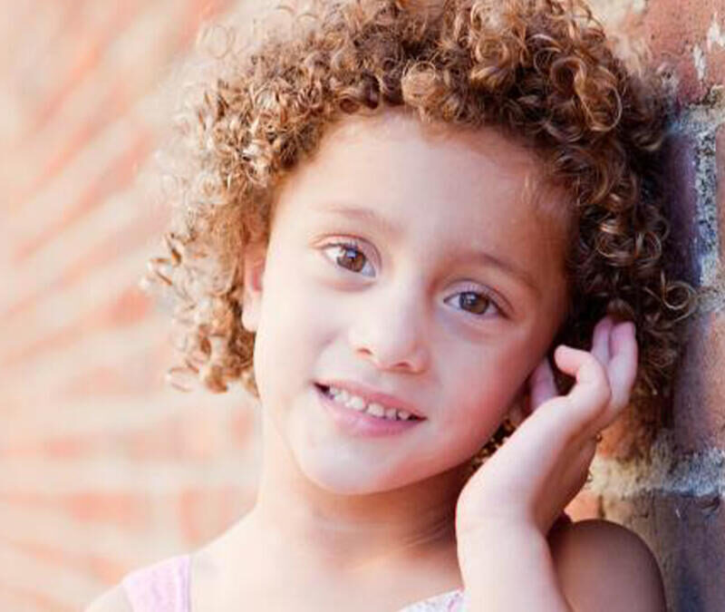 A little girl leaning against a brick wall.