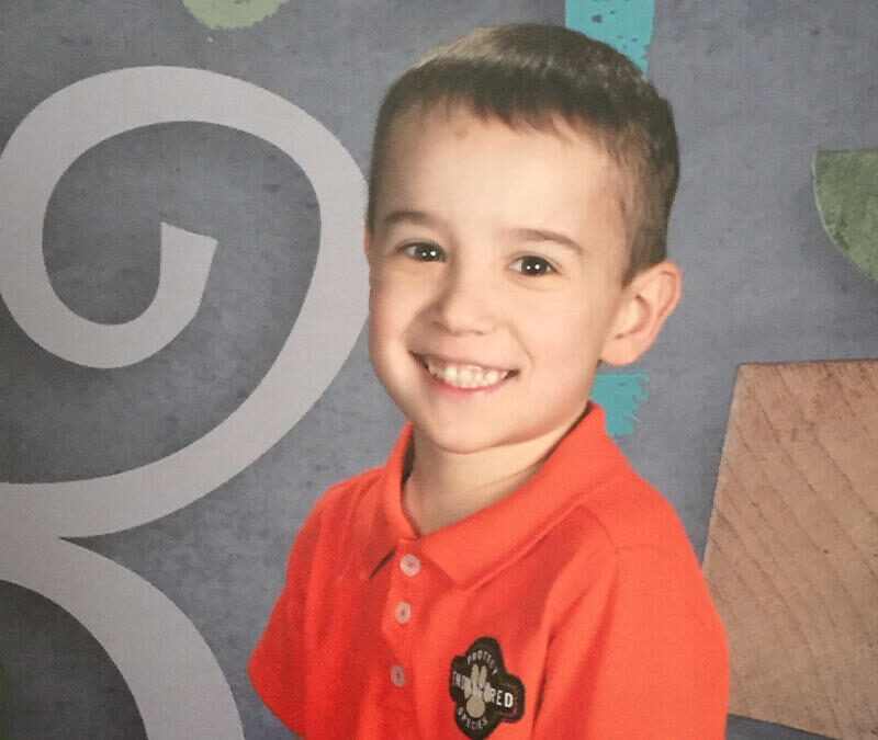 A young boy is posing for a photo in front of a chalkboard.