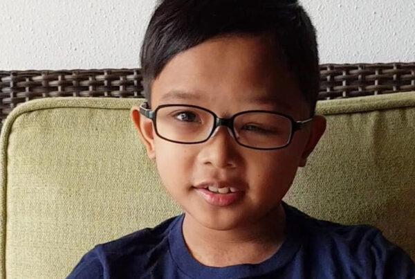 A young boy with glasses sitting on a couch.