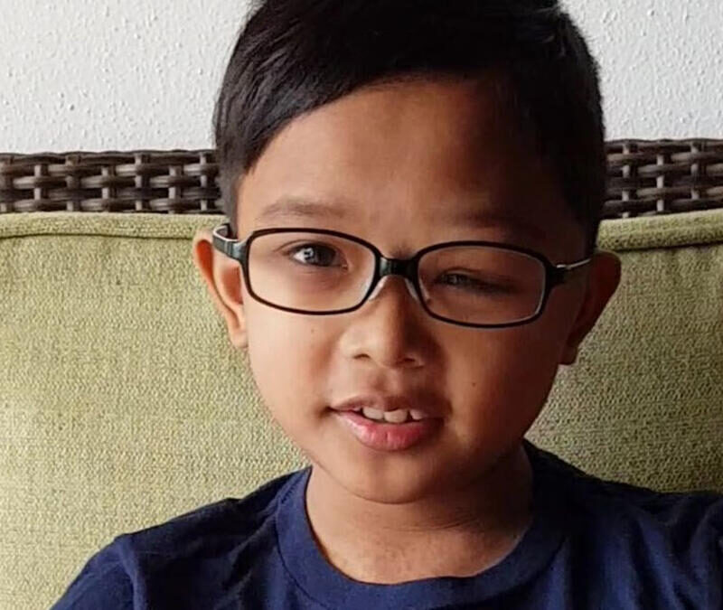 A young boy with glasses sitting on a couch.