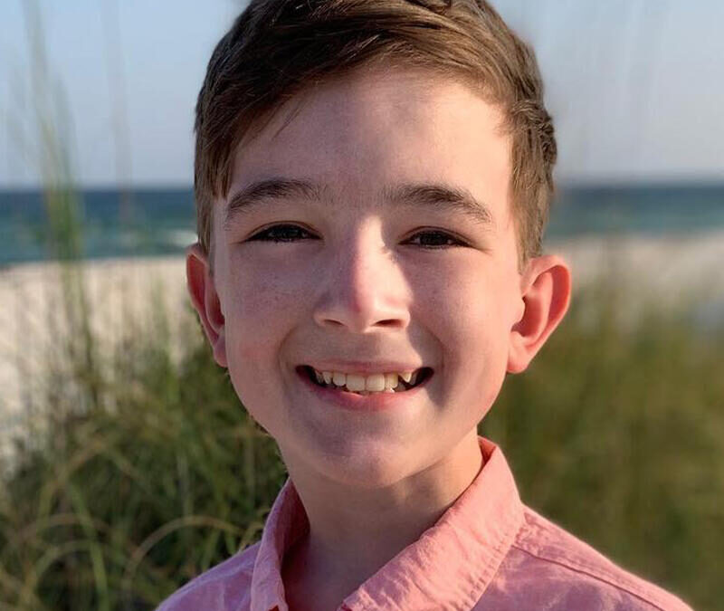 A young boy smiling in front of the ocean.