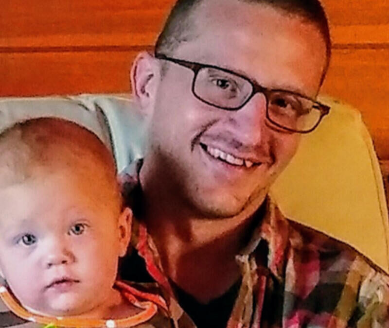 A man with glasses holding a baby in a chair.
