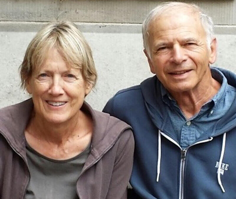 A man and woman are sitting on a bench in front of a building.