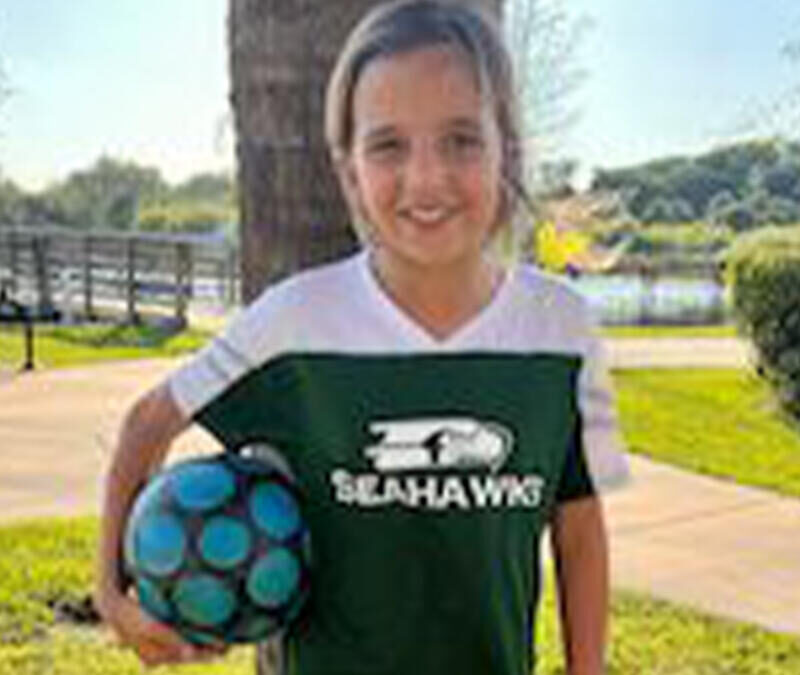 A young girl holding a soccer ball in a park.