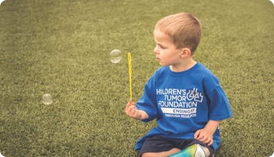 A young boy blowing bubbles on the grass.