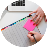 A woman writing on a sticky note on a desk.