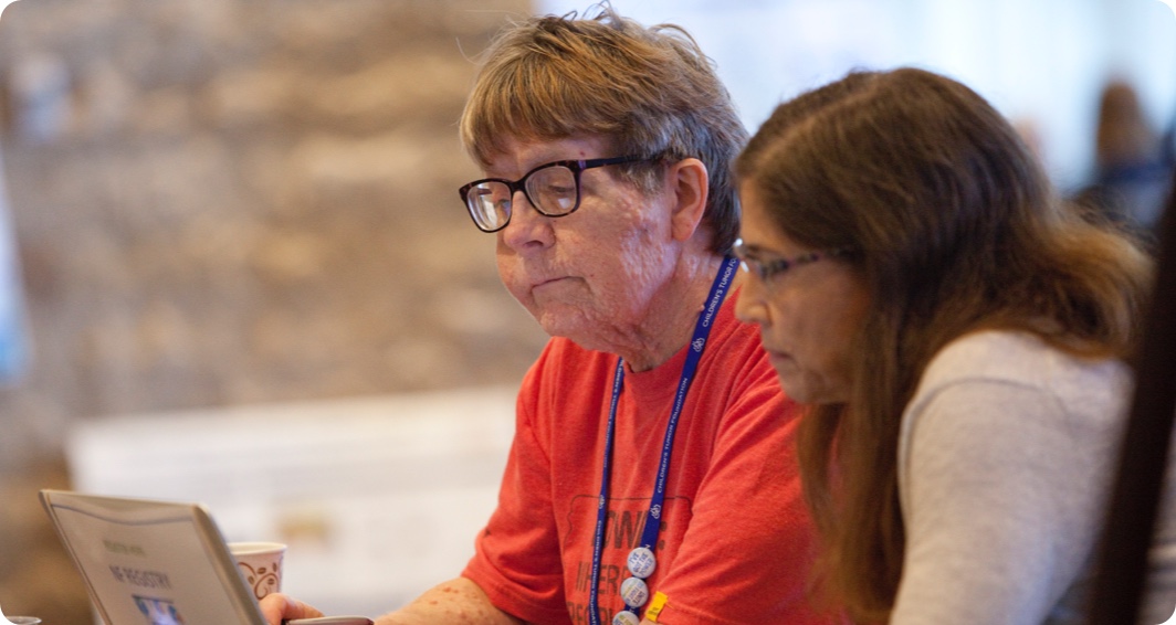 Two women sitting at a table looking at a laptop.