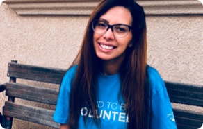 A woman wearing glasses and a t - shirt sitting on a bench.