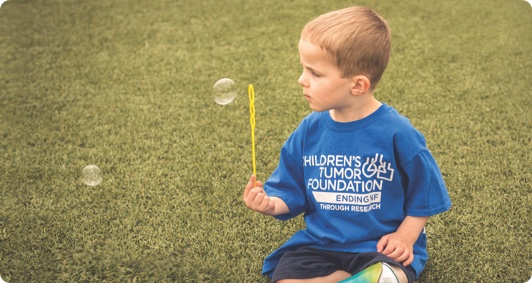 A young boy playing with soap bubbles on the grass.