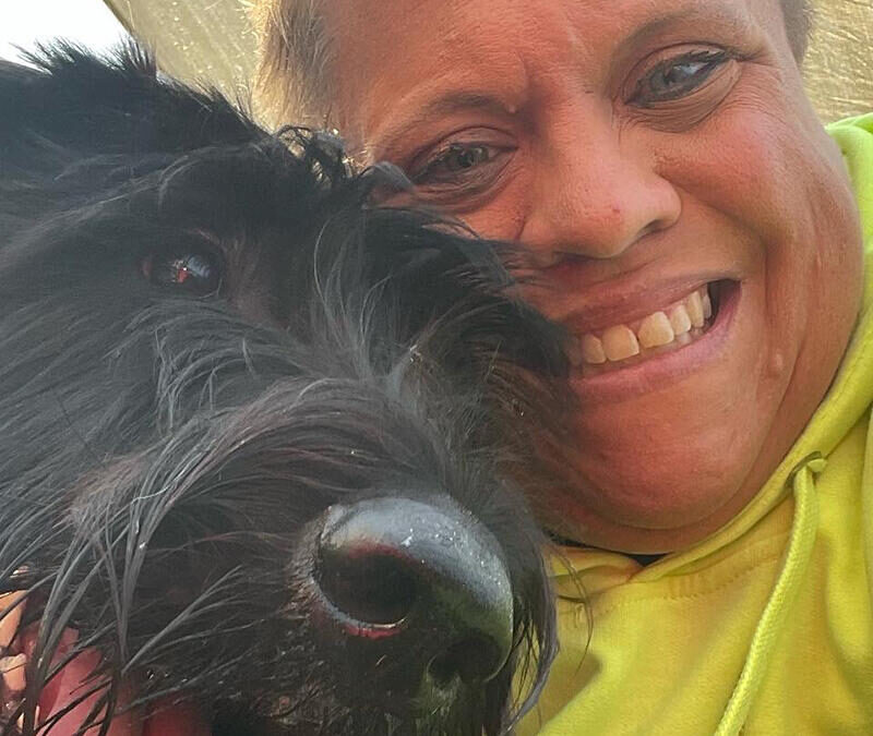 A woman in a green hoodie with a black dog.