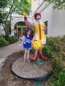 A little girl standing next to a mcdonald's statue.