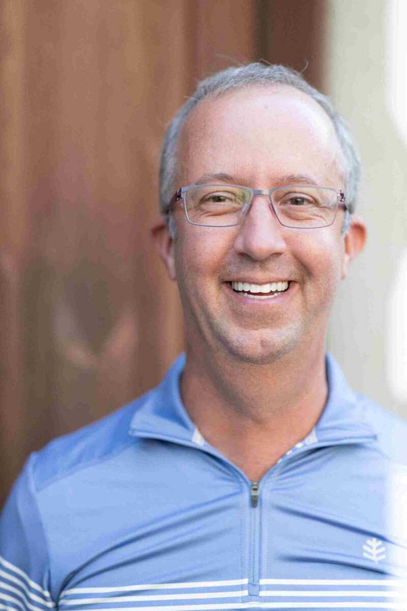 A smiling man wearing glasses and a blue polo shirt.