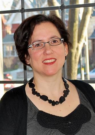 A woman in glasses is smiling in front of a window.