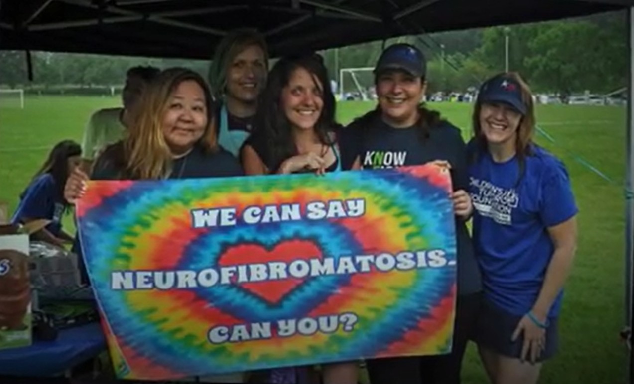Four women holding a tie-dye sign that says, "we can say neurofibromatosis can you?"