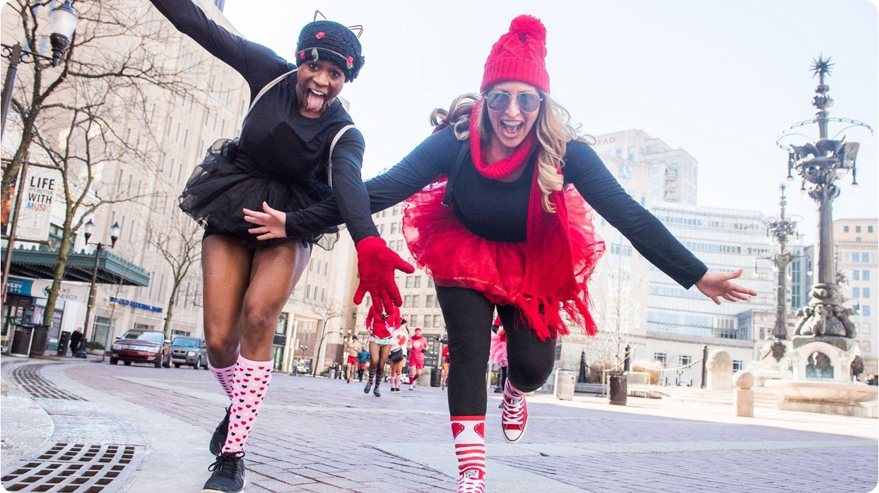 Two women dressed in red and white running on a city street.