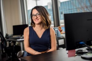 A woman in glasses sitting at a desk in an office.