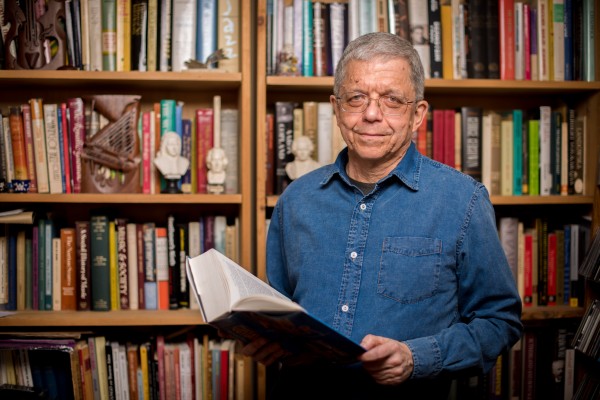 A man holding a book in front of a book shelf.