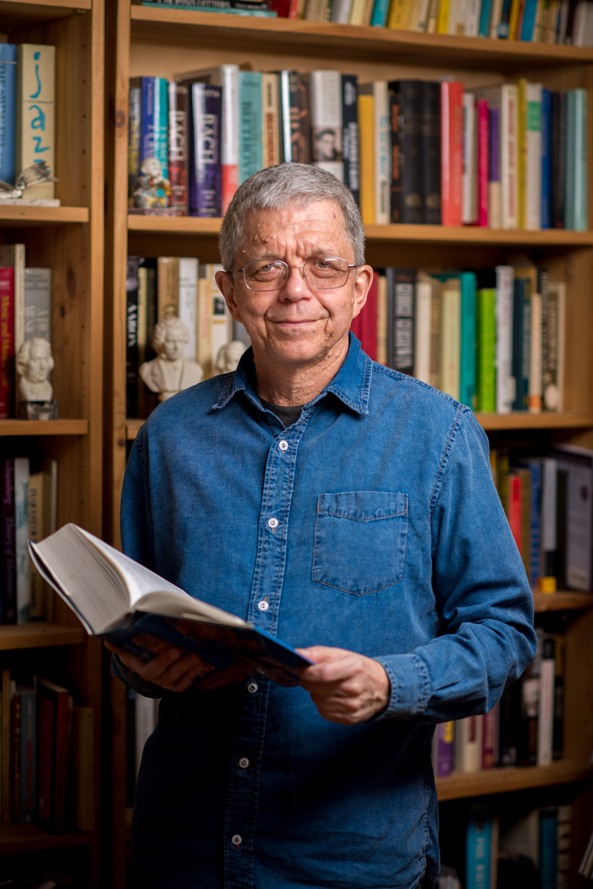 A man holding a book in front of a book shelf.