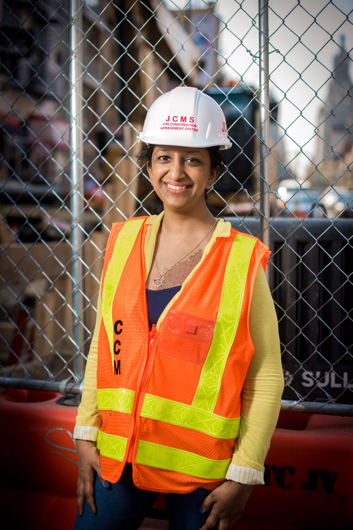 A woman wearing a hard hat and orange vest in front of a construction site.