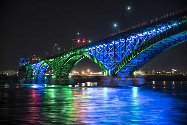A bridge is lit up at night with blue and green lights.
