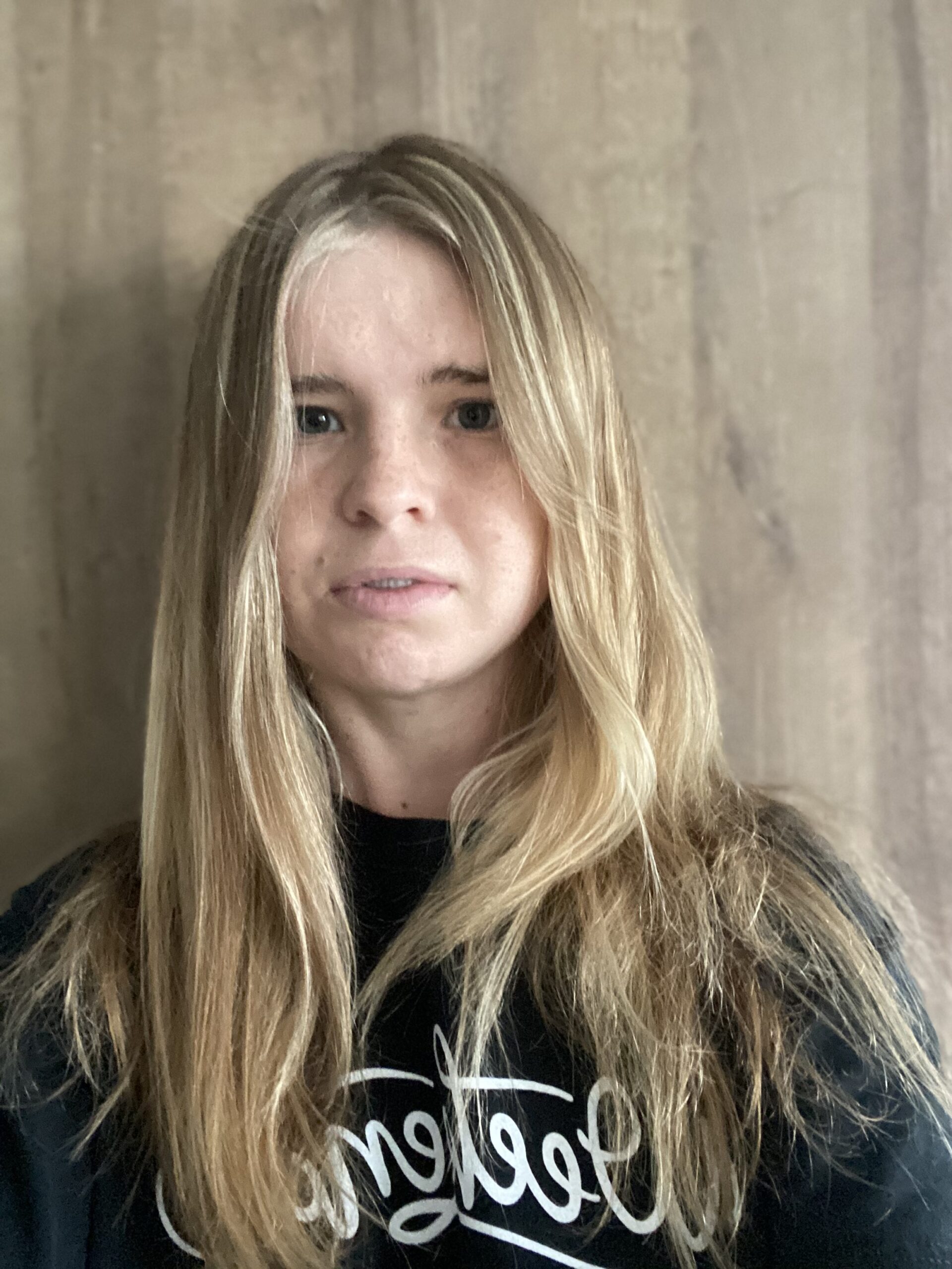 A woman with long blonde hair standing in front of a wall.