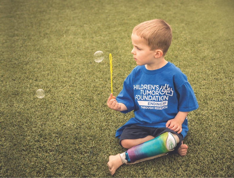 A young boy blowing bubbles on the grass.