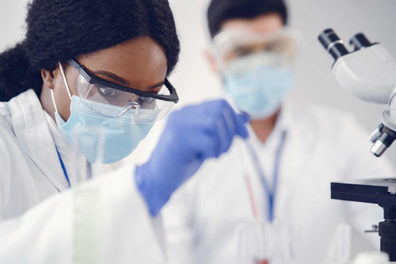 Two people in lab coats working on a microscope.