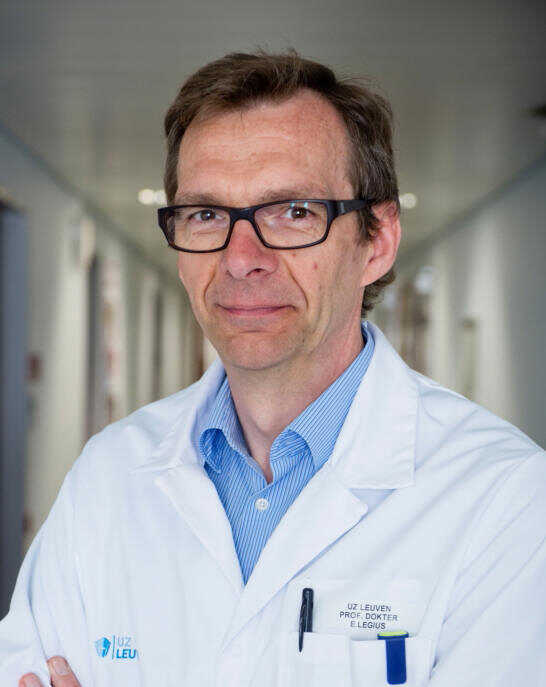 A man in a white lab coat standing in a hallway.