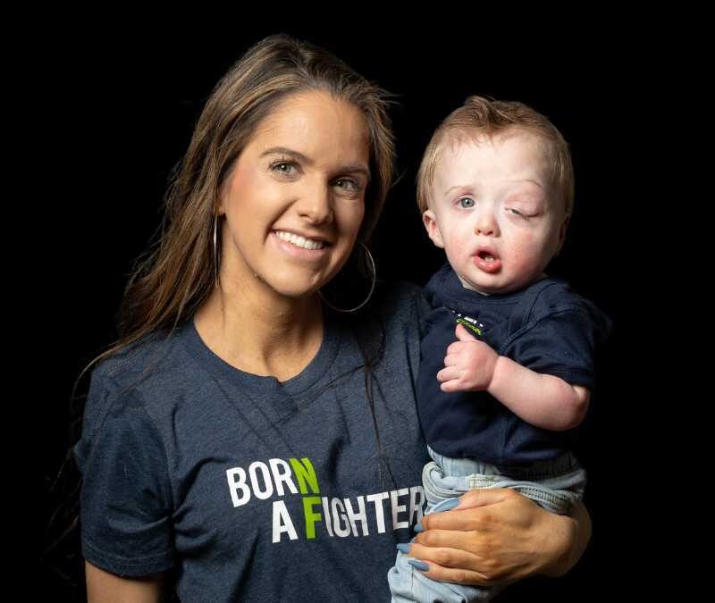 A woman holding a baby with a t - shirt that says born a fighter.