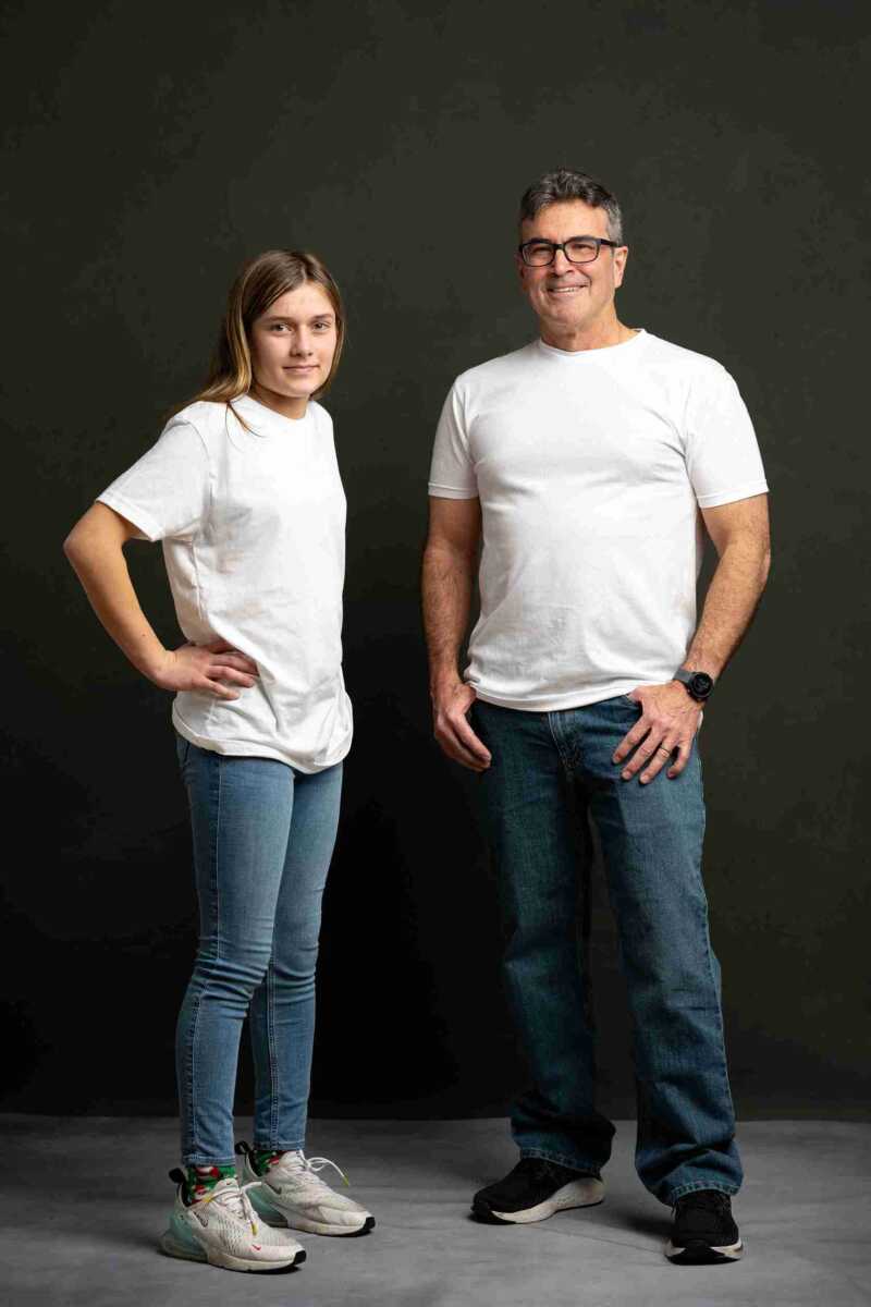 A man and woman in white t - shirts standing in front of a black background.
