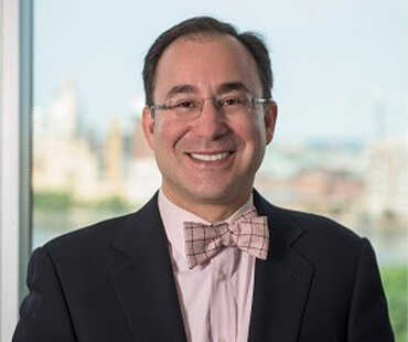 A man in a suit and tie smiling in front of a window.