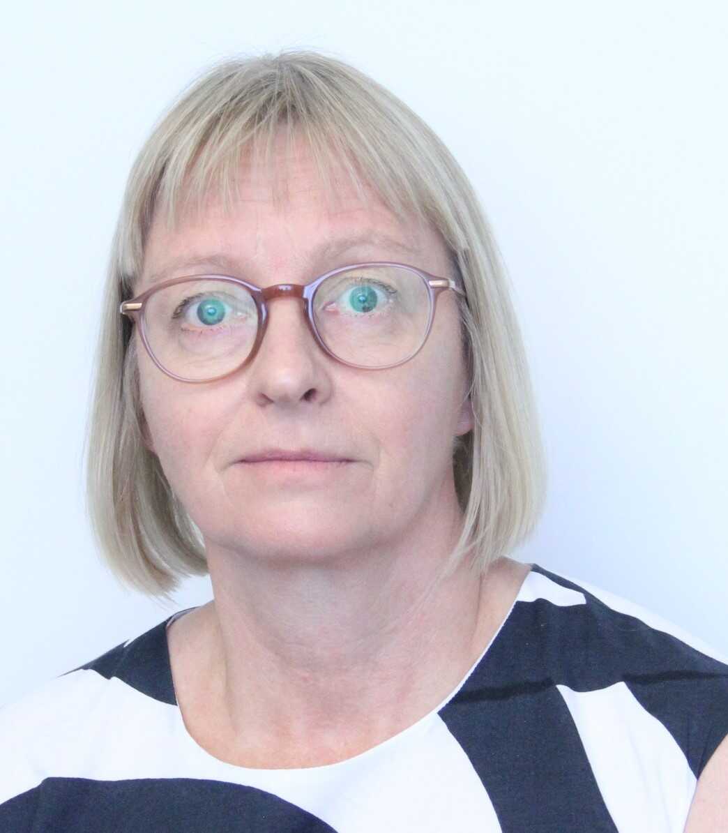 A woman in glasses is standing in front of a white wall.