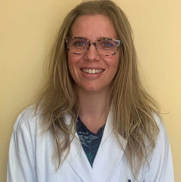 A woman in a lab coat smiling in front of a yellow wall.