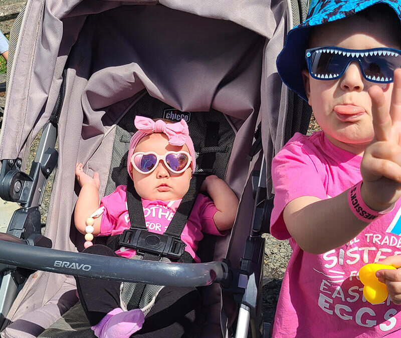 A baby in a stroller with sunglasses and a peace sign.
