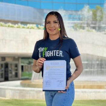 A woman holding a certificate in front of a fountain.