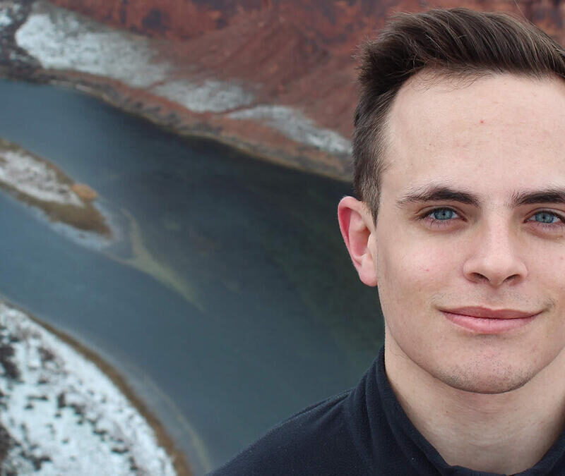 A young man is standing in front of a river.