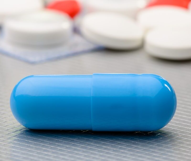 A close-up of a blue capsule pill on a surface with other pills in the background.