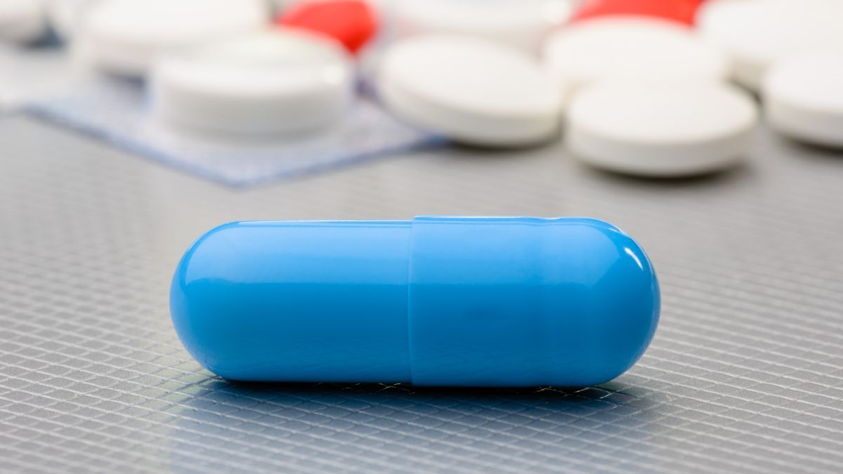 A close-up of a blue capsule pill on a surface with other pills in the background.