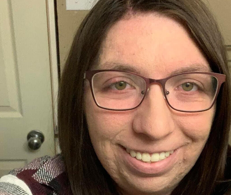 A woman with glasses smiling at the camera in a room with a closed door in the background.