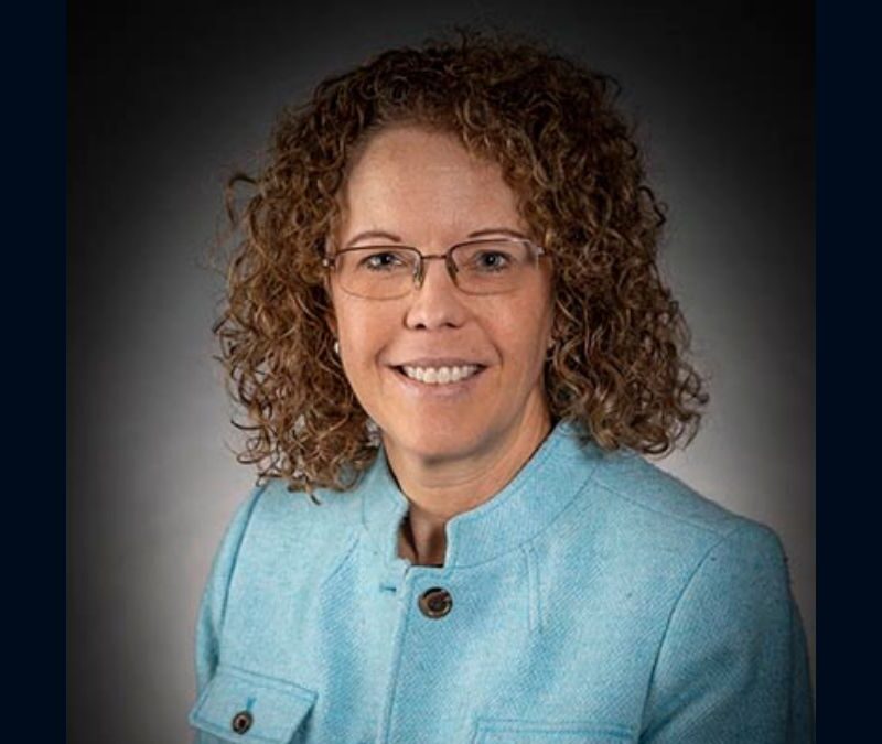 Professional portrait of a woman with curly hair wearing glasses and a blue blazer.