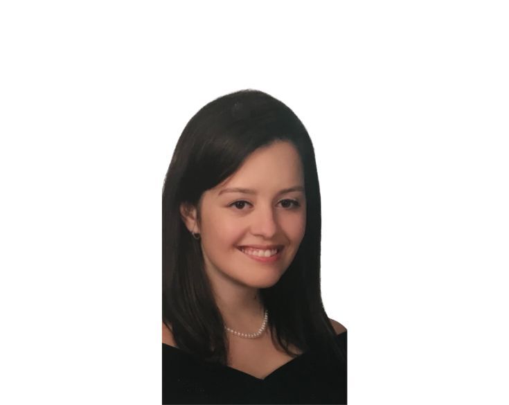 Portrait of a smiling woman with long dark hair, wearing a black top and a pearl necklace, against a plain white background.