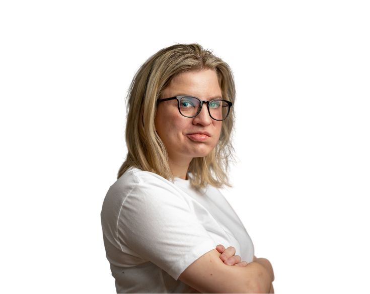 A woman with blonde hair wearing glasses and a white shirt, arms crossed, looking skeptically to the side against a white background.