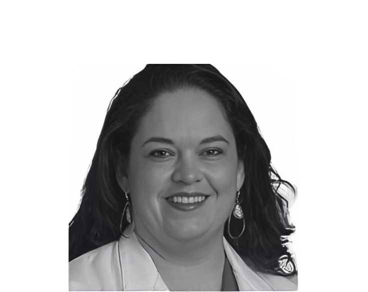 A black and white portrait of a smiling woman with shoulder-length hair wearing earrings and a light-colored blazer.