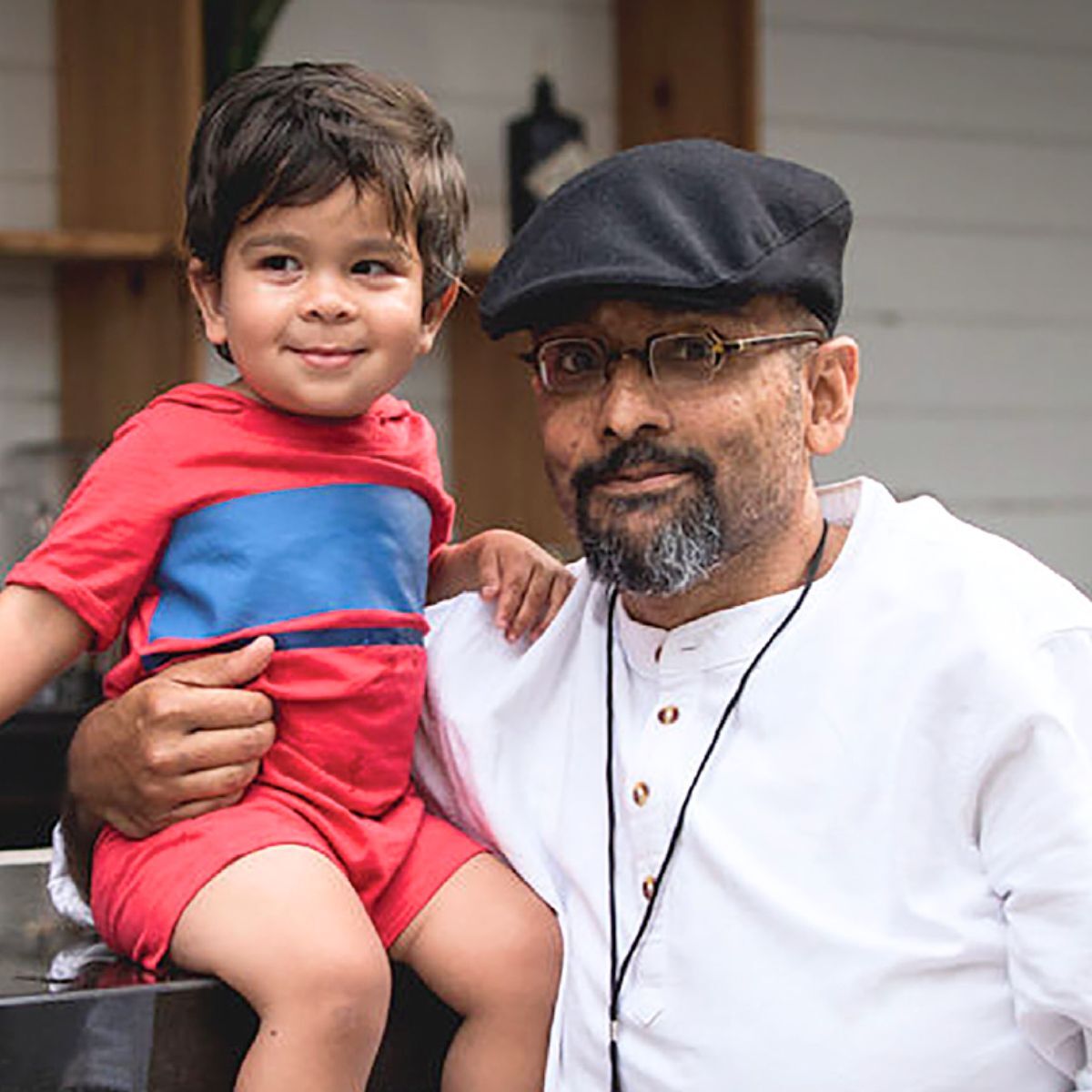 A man with glasses and a cap holding a young child in a red and blue outfit.