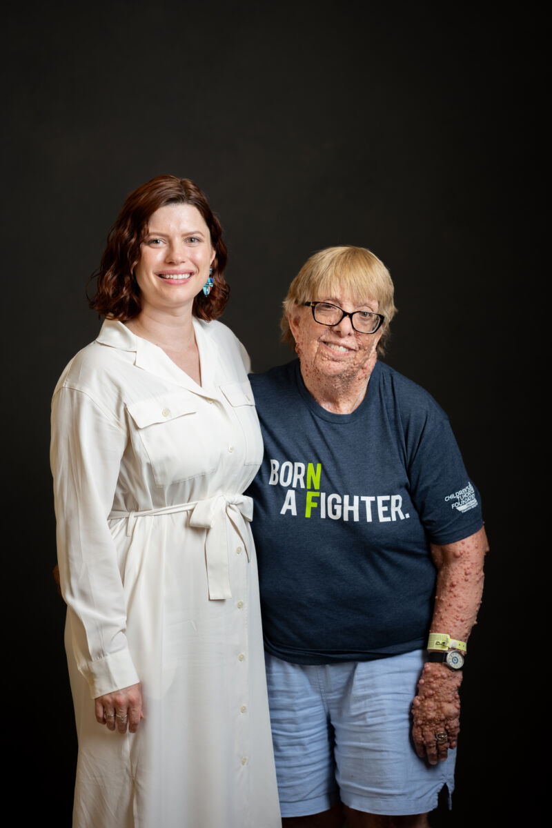 Two people posing for a photo, one wearing a shirt with the text "born a fighter.