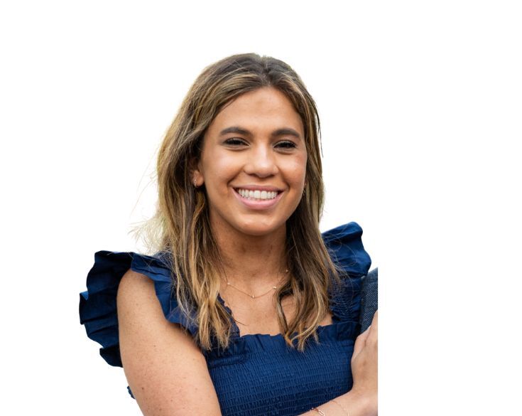 A smiling woman in a blue ruffled top, arms crossed, with a white background.